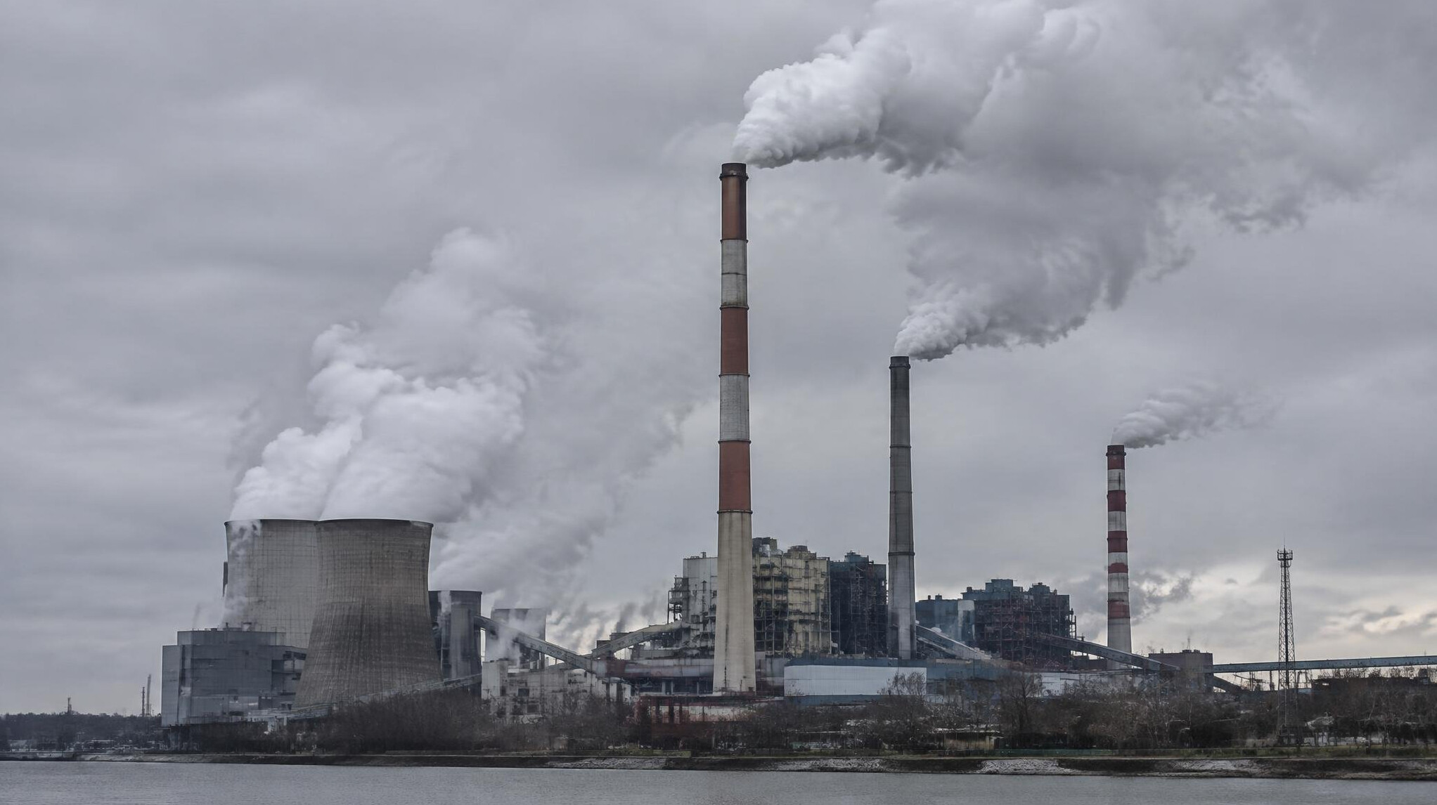 Industrial smoke stacks emitting exhaust against a grey sky