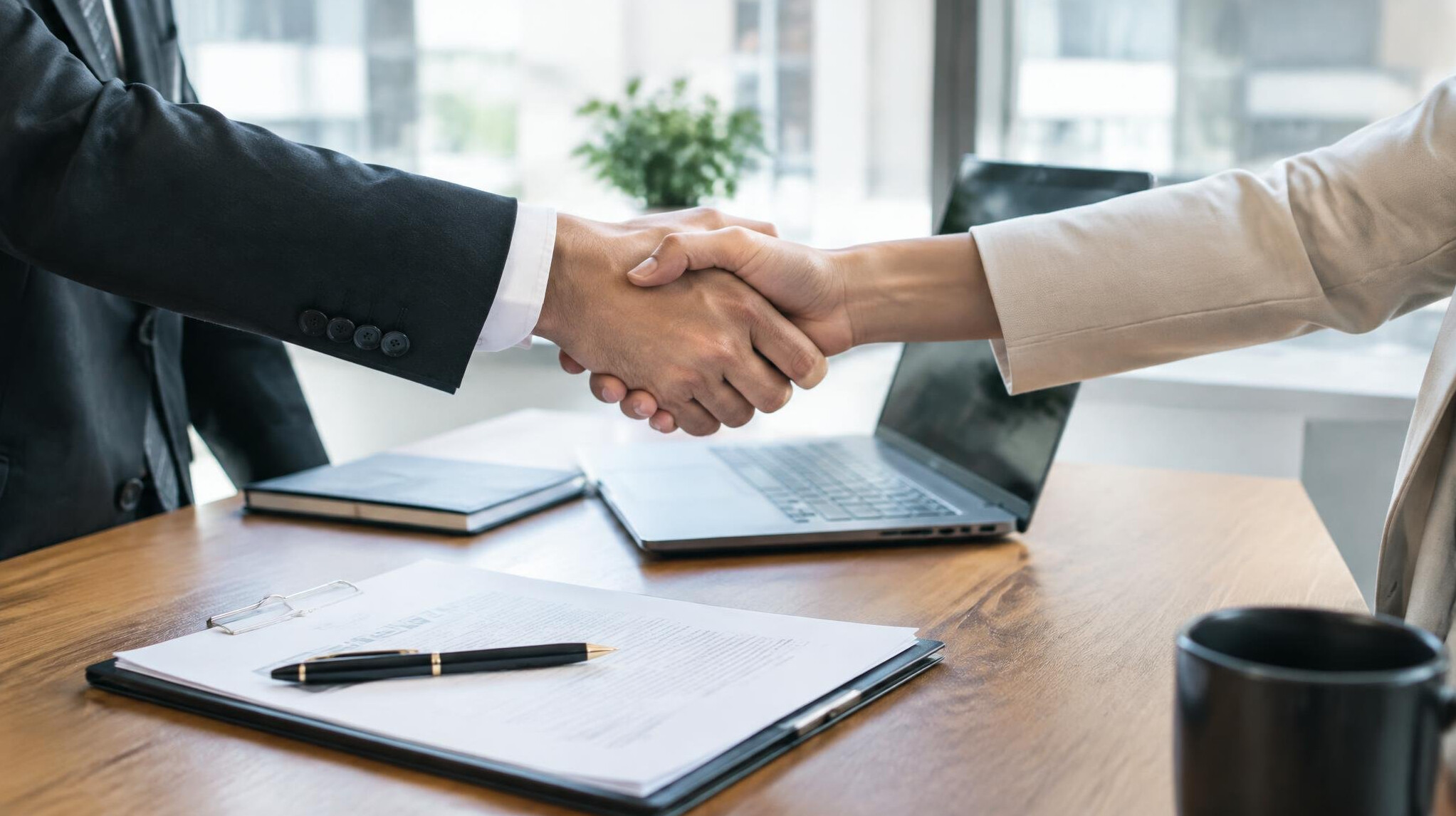 Two people shaking hands over a table with documents